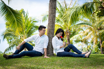 Young happy lovely couple sitting in the green park. Under the coconut tree. Man giving red roses to Young women.