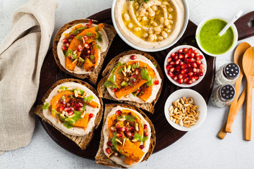 snack breads with hummus and baked pumpkin on a serving board with arugula pesto. seeds of pomegranate and pine nuts. healthy food