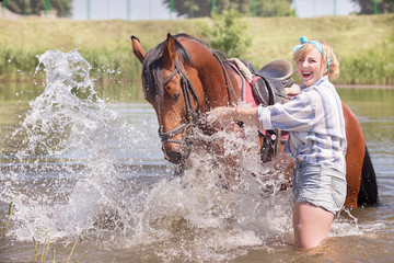 Fototapeta na wymiar Cheerful, beautiful blonde girl walks in summer sunny weather in a forest by the river with a horse