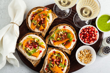 tasty bruschettes with hummus, baked pumpkin and arugula pesto on the table. vegan healthy food served with white wine