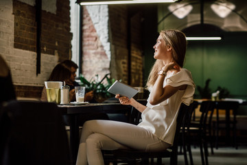 Young blond lady drinking coffe and looking aside through a window. in modern cafe interior.