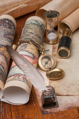 Quill pen on old paper sheets with old rolled maps and vintage items