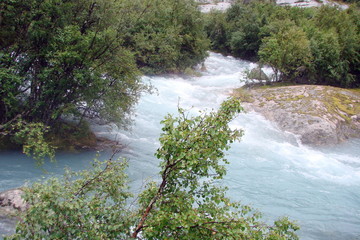 view of a crystal clear river flowing between the rocks from the melting glacier.