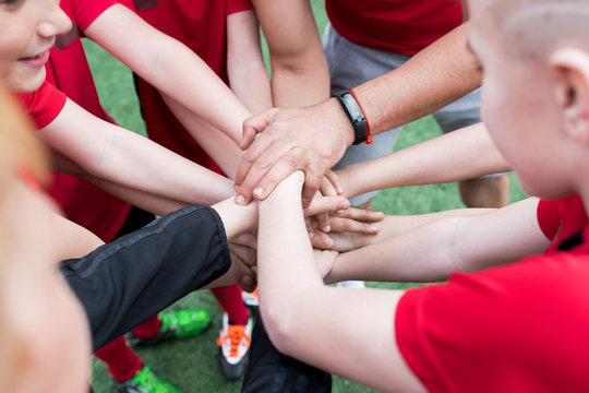 High angle closeup of junior football team stacking hands during motivational pep talk before match in outdoor stadium, copy space