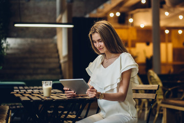 Young blond lady drinking coffe and working with tablet in modern club or dark cafe modern interior.