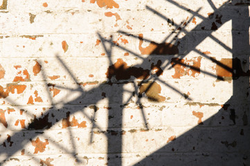 Shadow of security spikes on top of a wall, on a whitewashed brick wall with paint peeling/flaking off.