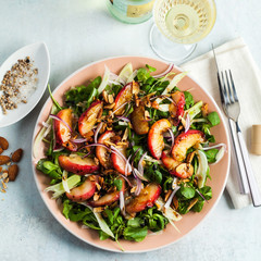 summer, very tasty salad with peaches, sweet onions and arugula with almonds on a table in a plate. simple healthy recipe and a bottle with a glass of white wine