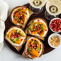 snack breads with hummus and baked pumpkin on a serving board with arugula pesto. seeds of pomegranate and pine nuts. healthy food