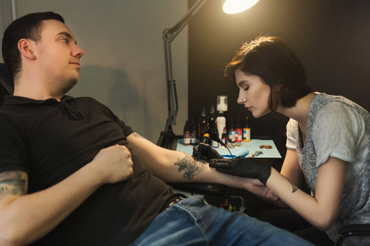 Young woman tattooist doing tattoo on male arm
