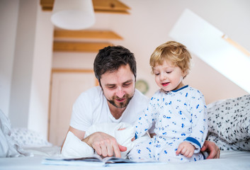 Father with toddler boy reading a book on bed at home at bedtime.
