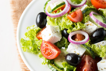 Fresh Greek salad made of cherry tomato, ruccola, arugula, feta, olives, cucumbers, onion and spices. Caesar salad in a white bowl on wooden background. Healthy organic diet food concept.