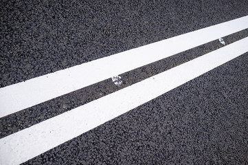 Fototapeta premium Two white solid lines on a new asphalt road. Close-up.