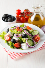 Fresh Greek salad made of cherry tomato, ruccola, arugula, feta, olives, cucumbers, onion and spices. Caesar salad in a white bowl on wooden background. Healthy organic diet food concept.