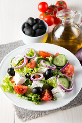 Fresh Greek salad made of cherry tomato, ruccola, arugula, feta, olives, cucumbers, onion and spices. Caesar salad in a white bowl on wooden background. Healthy organic diet food concept.