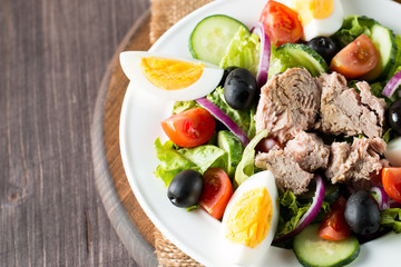 Fresh fish tuna salad made of tomato, ruccola, tuna, eggs, arugula, crackers and spices. Caesar salad in a white bowl on wooden background