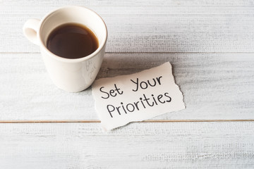 Set your priorities reminder handwriting on a paper note with a cup of espresso coffee.