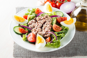 Fresh fish tuna salad made of tomato, ruccola, tuna, eggs, arugula, crackers and spices. Caesar salad in a white bowl on wooden background