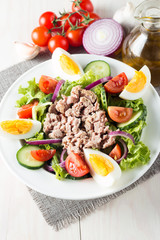 Fresh fish tuna salad made of tomato, ruccola, tuna, eggs, arugula, crackers and spices. Caesar salad in a white bowl on wooden background