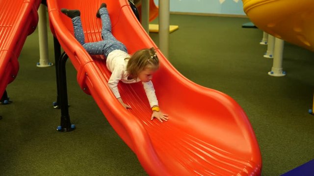 Funny little child girl enjoy sliding down and crowling up on a slide on indoors playground