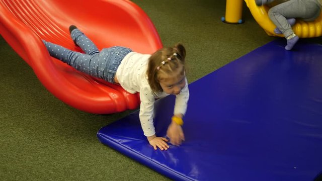 Funny little child girl enjoy sliding down and crowling up on a slide on indoors playground