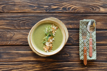 top view of bowl of vegetarian cream soup with broccoli, sprouts and almonds on wooden surface
