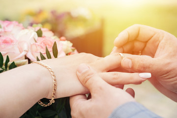 groom puts the ring on the bride's hand sunset