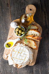 Baked camembert cheese. Fresh Brie cheese and a slice on a wooden board with nuts, honey, rosemary, baguette bread grilled toasts and leaves. Brie type of cheese. Italian, French cheese.