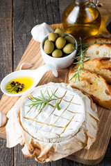 Baked camembert cheese. Fresh Brie cheese and a slice on a wooden board with nuts, honey, rosemary, baguette bread grilled toasts and leaves. Brie type of cheese. Italian, French cheese.