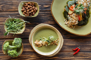 flat lay with arrangement of vegetarian salad, cream soup and ingredients around on wooden surface