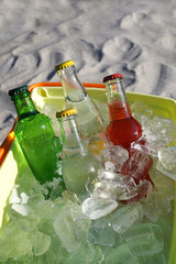 Cold soda drinks, filled ice cubes in a coolbox on the beach sand.