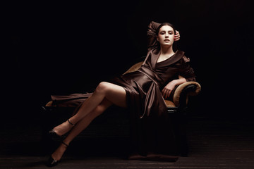 The girl in the brown dress. Sitting on a couch in the Studio. Black background.