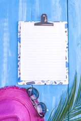Blue wooden background, pink hat, palm branch, sunglasses place for text in the center. Summer time. Copy space, flat lay.