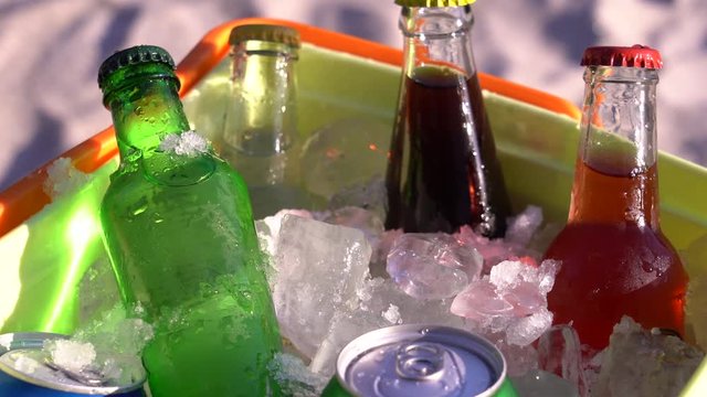 Soda drinks and filled ice cubes in a coolbox on the beach sand. 4K video