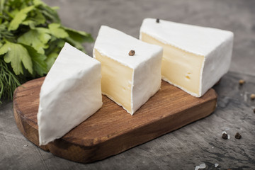 Three soft cheeses with white mold on a wooden cutting board