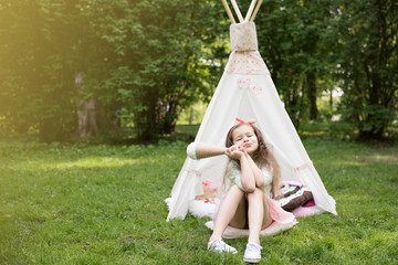 Little girl playing in a tent, children's house wigwam in park. Happy mothers day. Child with big donuts and ice cream and straw hat Summer, happy childhood concept. Cute emotions girl. © MartaKlos
