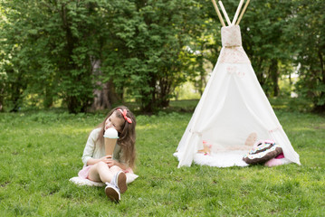 Little girl playing in a tent, children's house wigwam in park. Happy mothers day. Child with big donuts and ice cream and straw hat Summer, happy childhood concept. Cute emotions girl. © MartaKlos
