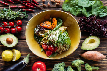 flat lay with vegetarian salad with grilled vegetables, sprouts, cherry tomatoes in bowl and arranged fresh ingredients around on wooden tabletop