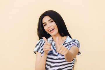 Shot of attractive European female gives double thumb up, has positive expression, has white teeth...