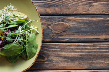 top view of vegetarian salad with spinach and sprouts on plate on wooden tabletop