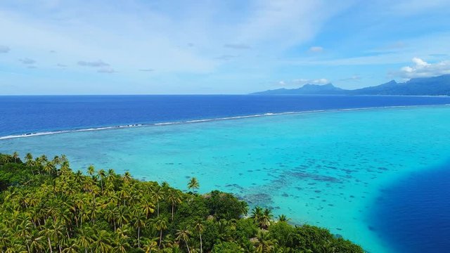Aerial view of coral barrier reef of Tahaa island, palm trees on islet Motu Atger and clear water of blue lagoon, Raiatea on background - South Pacific Ocean, seascape of French Polynesia from above