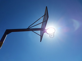 The bright sun shines through the basket of the basketball ring against the background of the clear blue sky.Modern basketball court in the courtyard of primary school. Place of physical education