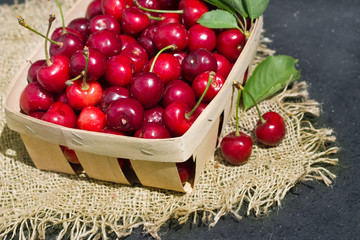 ripe red cherry berries in a wooden wicker package on a background of matting