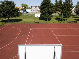 Fototapeta premium Modern basketball court under the open sky with artificial red coating. Location of team sports events. Physical education of citizens. Healthy lifestyle. Urban infrastructure for recreation, interest