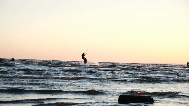 Kitesurfer does a trick with a board on the sea at sunset in summer, slow motion