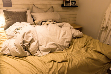 Dirty bed with white pillows and white blanket in the room