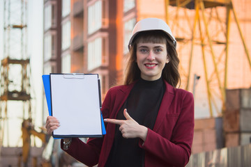 Woman holding blueprints, clipboard. Smiling architect in helmet at building