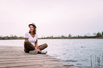 Fototapeta premium Young woman sitting on wooden pier, relaxing.