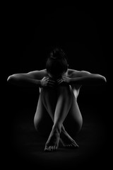 Art nude, perfect naked body, sexy woman sitting on dark background, black and white studio shot