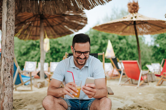 Smiling young man using smartphone while relaxing at the beach.