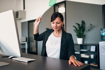 Businesswoman with flyswatter sitting at desk.